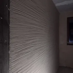 Świeżo położony tynk dekoracyjny na ścianie wewnętrznej, z wyraźną fakturą przypominającą fale, widoczny róg pomieszczenia i fragment okna.