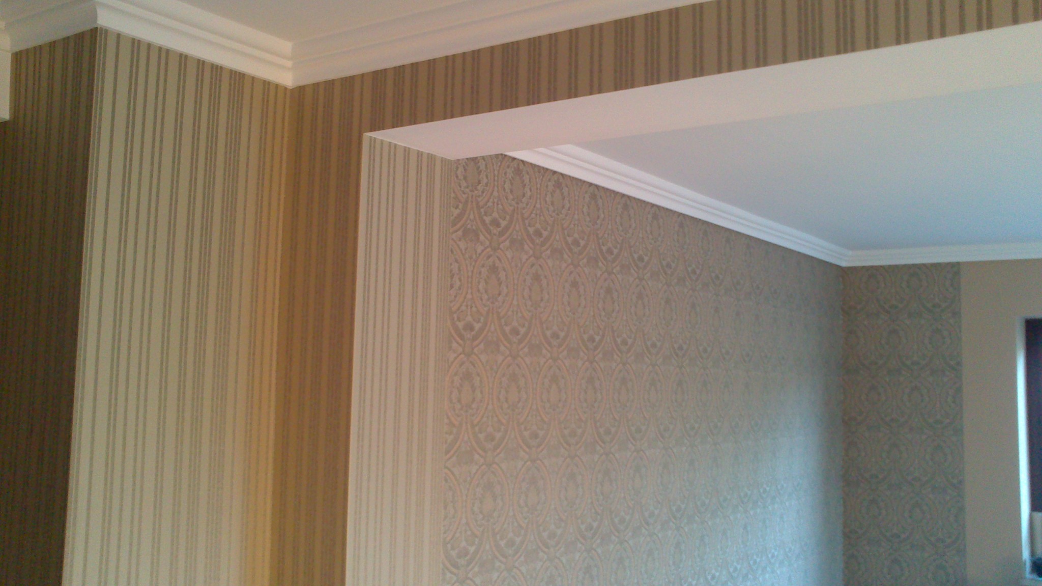 Wykończone wnętrze z tapetami w dwóch wzorach: pionowe pasy i ornamenty. Biały sufit z dekoracyjnym gzymsem. Neutralna kolorystyka, ciepłe odcienie beżu i brązu.