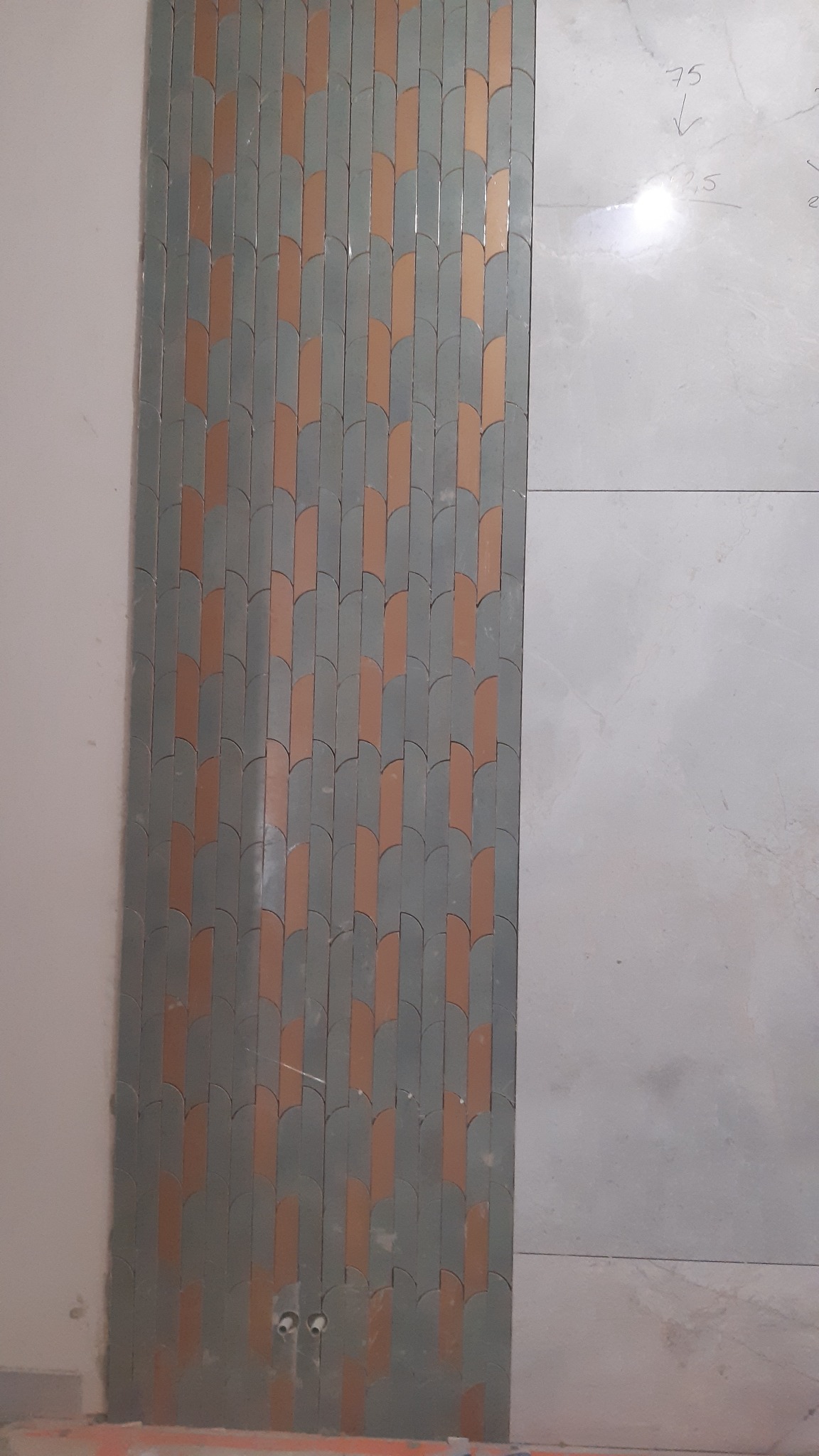 Ukończona ściana z dekoracyjną mozaiką w odcieniach szarości i miedzi, sąsiadująca z jasną płytą. Widoczne niedoskonałości przy podłodze.