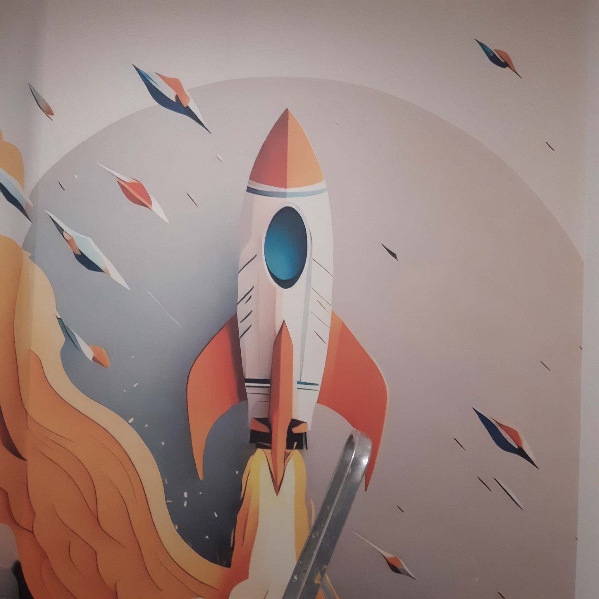 Dziecięcy pokój z tapetą: rakieta kosmiczna w locie, pomarańczowo-biała kolorystyka, delikatne tło z motywem kosmosu. Widoczny fragment drabiny.
