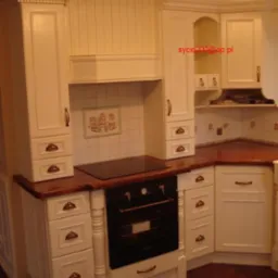 Klasyczna kuchnia z kremowymi szafkami z dekoracyjnymi uchwytami i blatem z ciemnego drewna, wyposażona w płytę grzewczą i piekarnik.