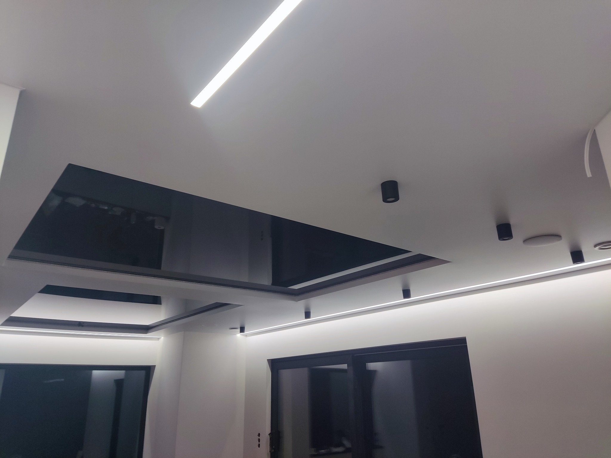 Nowoczesny sufit podwieszany z czarnym lustrzanym wkładem i oświetleniem LED liniowym oraz punktowym w minimalistycznym wnętrzu.