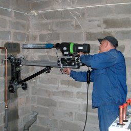 ENERGY PARTNER Bogdan Grala - Hydraulik wierci otwór w ścianie z bloków za pomocą wiertnicy diamentowej z zamocowanymi rurami miedzianymi. Widoczne ślady po wierceniu.