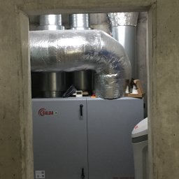 ENERGY PARTNER Bogdan Grala - Szara jednostka rekuperacyjna Salda RIRS 1900VER EKO w betonowym pomieszczeniu, z widocznymi srebrnymi kanałami wentylacyjnymi i fragmentem zmiękczacza wody.