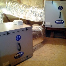 ENERGY PARTNER Bogdan Grala - Szara jednostka rekuperacji z widocznymi przewodami wentylacyjnymi w izolacji, zamontowana w pomieszczeniu technicznym. Widoczne logo firmy.