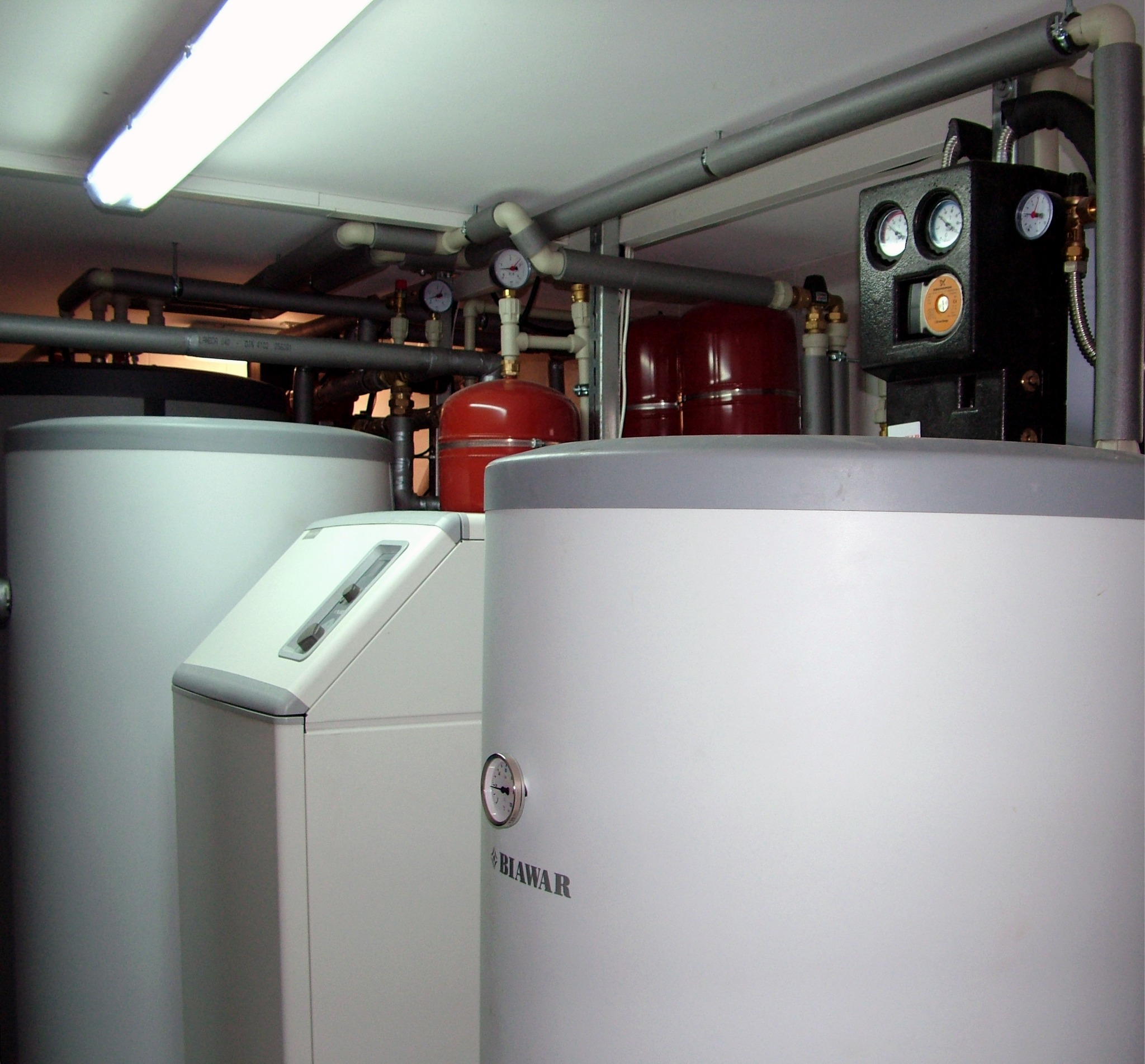 Instalacja grzewcza z zbiornikami Biawar i rozbudowaną siecią rur w Rozłogach. Widoczne manometry i elementy sterujące. Oświetlenie jarzeniowe.