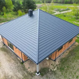 Nowy, grafitowy dach z blachodachówki na surowym budynku z cegły, widok z góry.