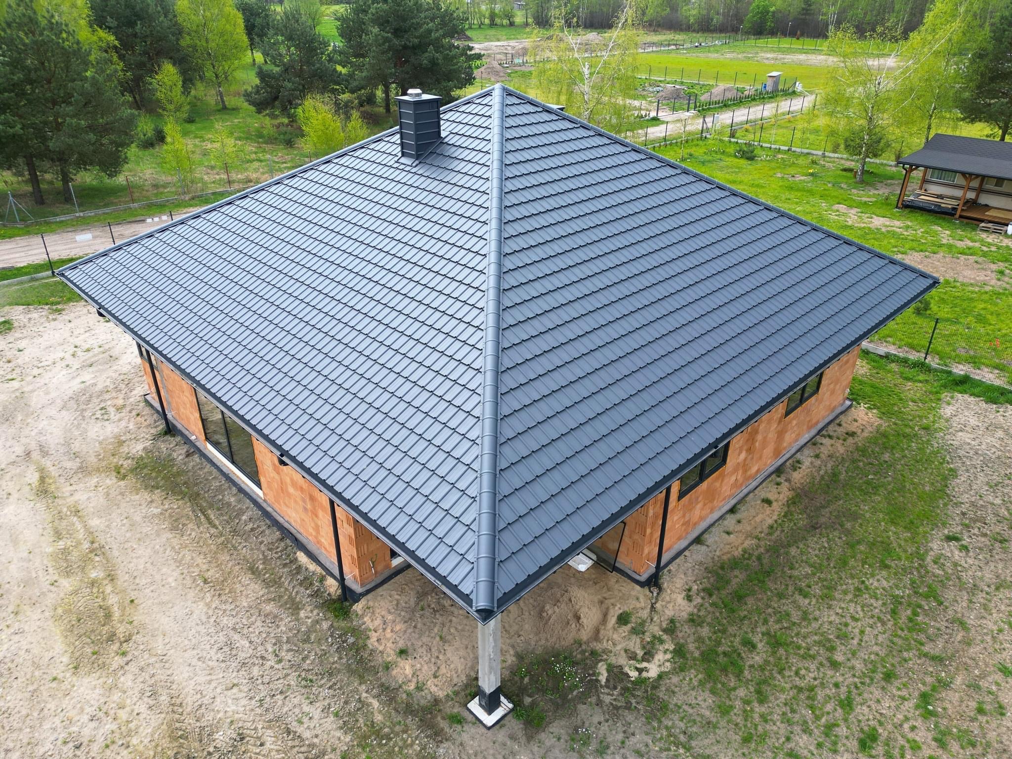 Nowy, grafitowy dach z blachodachówki na surowym budynku z cegły, widok z góry.