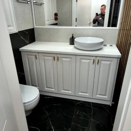 Extra Front s.c - Nowoczesna łazienka z czarną marmurową podłogą, białymi szafkami pod umywalką nablatową, lustrem z odbiciem osoby robiącej zdjęcie i wiszącymi lampami.