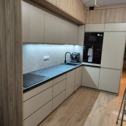 Extra Front s.c - Nowoczesna kuchnia z beżowymi szafkami i blatem w kolorze antracytu, oświetlenie LED pod szafkami, drewniana podłoga, widoczne niedokończone podłączenie elektryczne na suficie i drabina malarska.