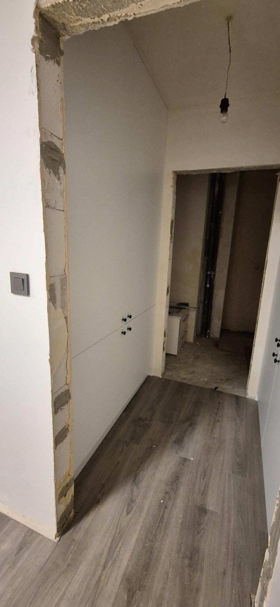 Wnętrze w trakcie remontu w Gomunicach: widoczne białe szafy z czarnymi uchwytami, surowe wykończenie ścian i podłoga imitująca drewno.