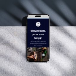 Antoni Wieloch - Ekran smartfona prezentujący mobilną wersję strony internetowej sklepu rybnego na tle betonowej powierzchni i ściany z cieniem.