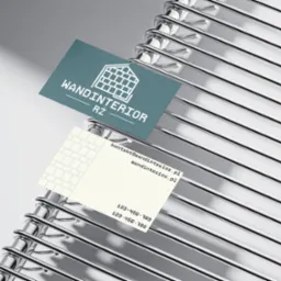 Dwie wizytówki firmy Wandinterior RŻ z motywem muru z cegieł, ułożone na chromowanym, metalowym stojaku na wizytówki.