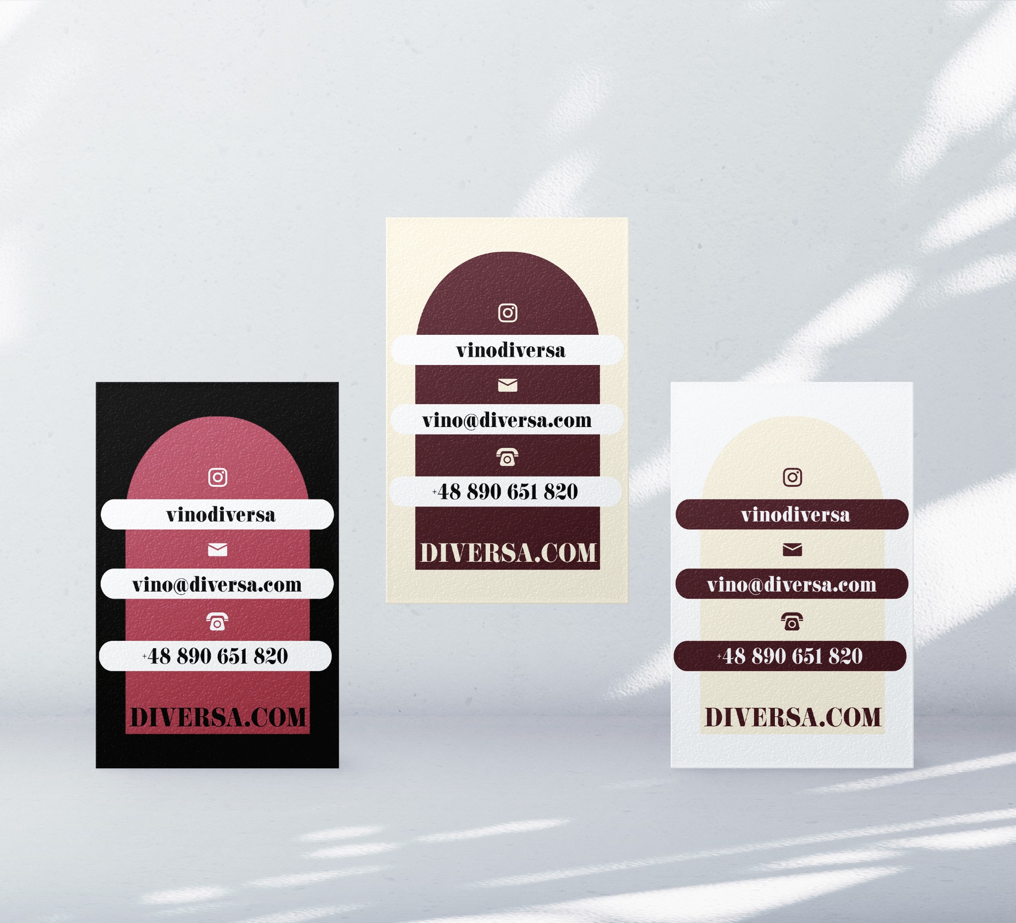 Trzy wizytówki z logo i danymi kontaktowymi firmy 'vinodiversa' w różnych wariantach kolorystycznych, ustawione na jasnym tle z cieniem liści.