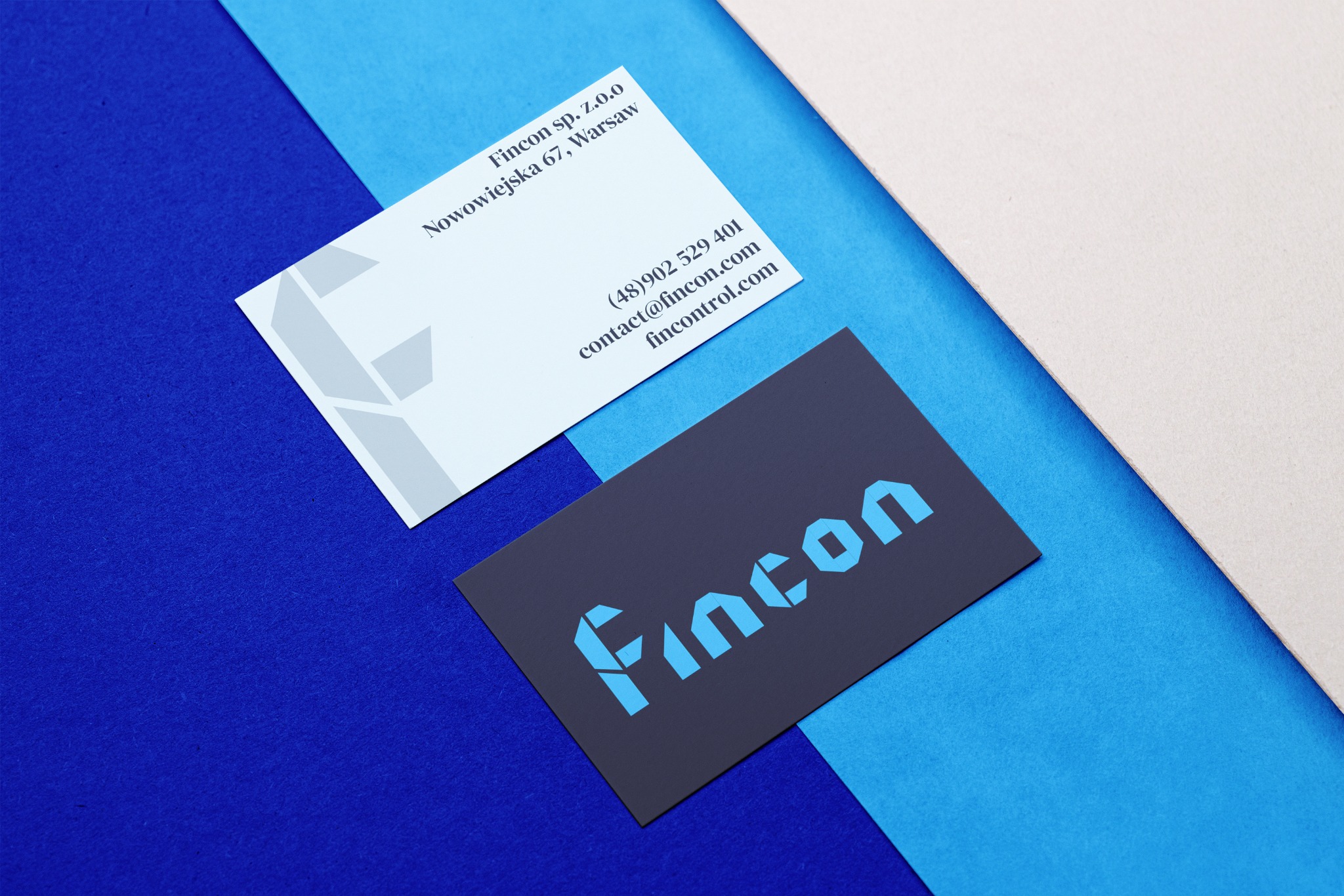 Dwie wizytówki firmy Fincon z Warszawy na tle w odcieniach niebieskiego i beżu. Jedna wizytówka jest jasna z szarym logo, druga ciemna z niebieskim logo.