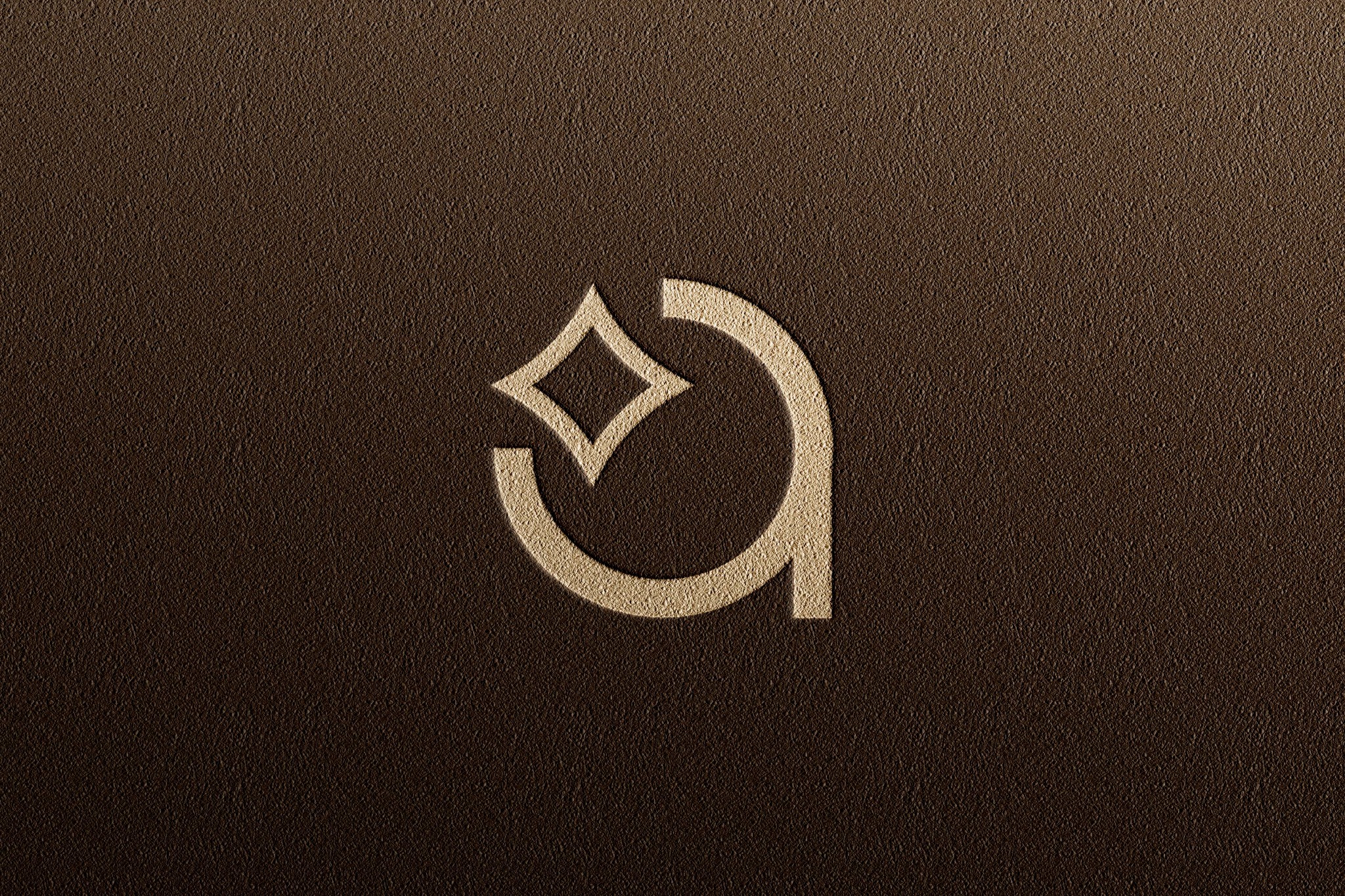Minimalistyczne logo: stylizowana litera 'a' z rombem zamiast górnej części, w kolorze złamanej bieli, wytłoczone na brązowym, teksturowanym tle.