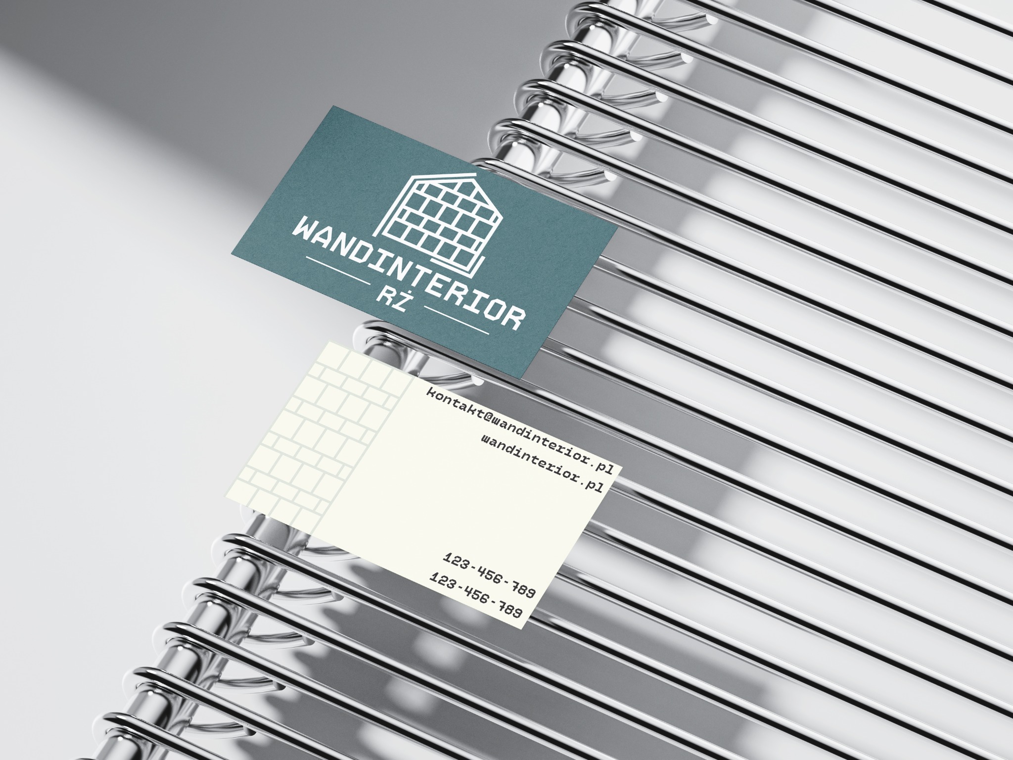 Dwie wizytówki firmy Wandinterior RŻ z motywem muru z cegieł, ułożone na chromowanym, metalowym stojaku na wizytówki.