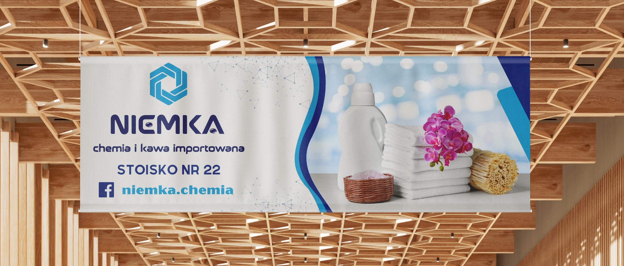 Baner reklamowy firmy Niemka z logo, adresem i zdjęciem produktu: butelka płynu, ręczniki, kwiat orchidei i koszyk z solą do kąpieli, wiszący na tle drewnianego sufitu.