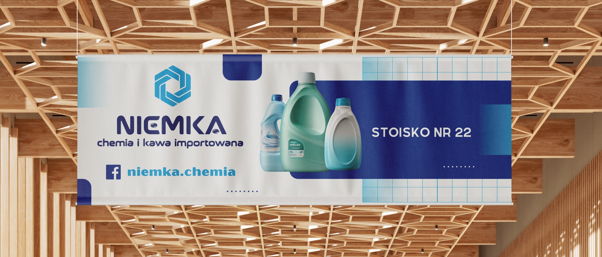 Baner reklamowy firmy 'Niemka' z chemią i kawą importowaną, wiszący pod drewnianym sufitem, prezentujący logo firmy, adres strony na Facebooku oraz wizualizację produktów czyszczących i numer stoiska.