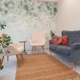 Jasne, przytulne wnętrze gabinetu z sofą, fotelami, dywanem i roślinami. Na ścianie tapeta w liście. Stonowana kolorystyka, relaksująca atmosfera.