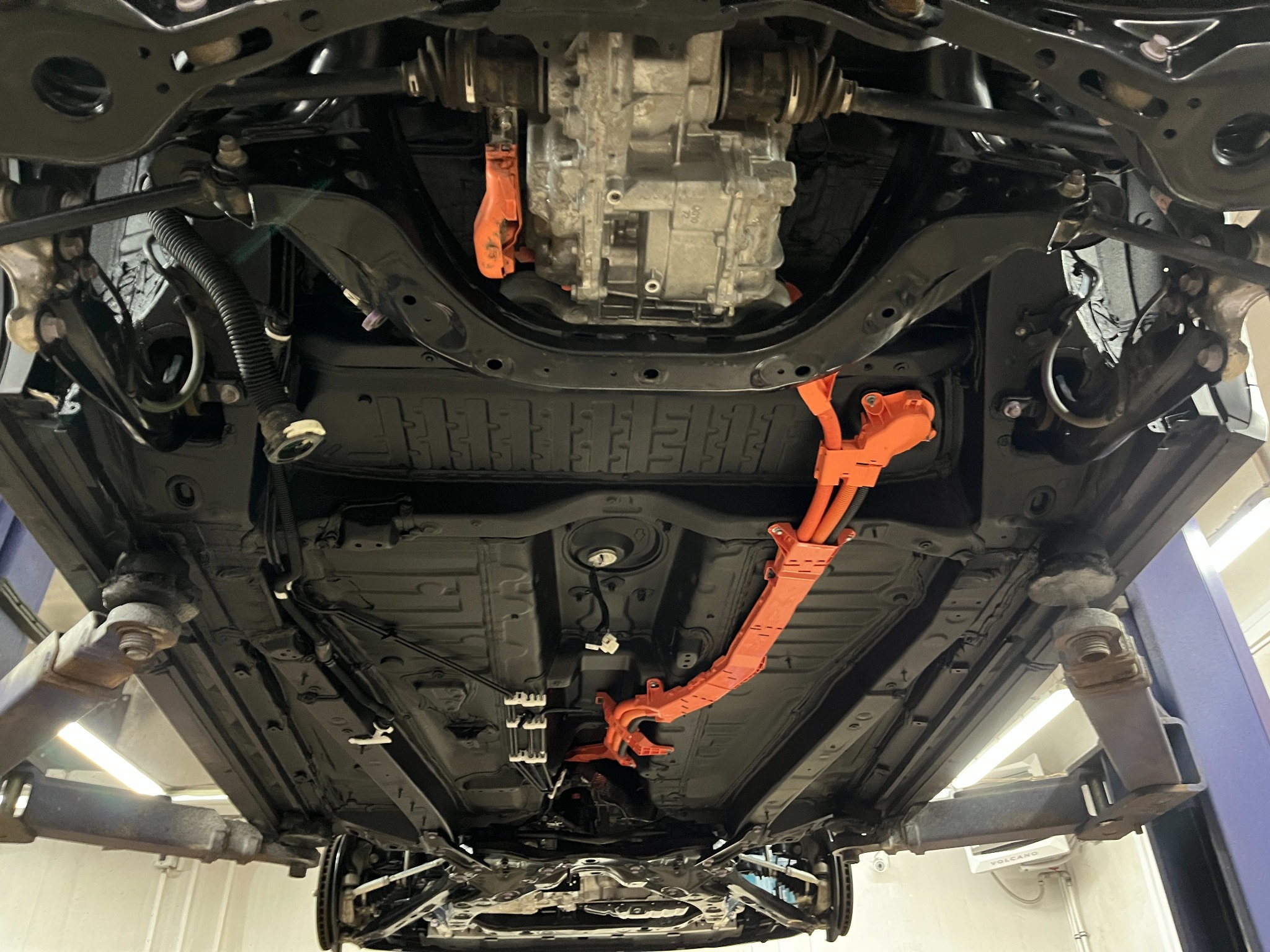 Podwozie samochodu po zabezpieczeniu antykorozyjnym w Młodocinie Mniejszym, widoczne elementy zawieszenia, układu wydechowego i przewody, pojazd uniesiony na podnośniku.