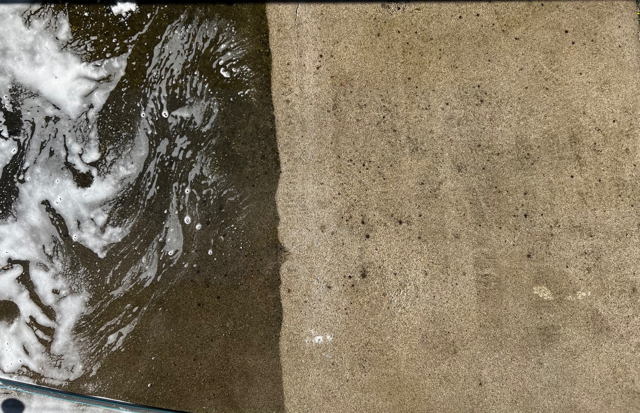 Częściowo umyta kostka brukowa z widoczną pianą i różnicą w kolorze pomiędzy czystą i brudną powierzchnią.