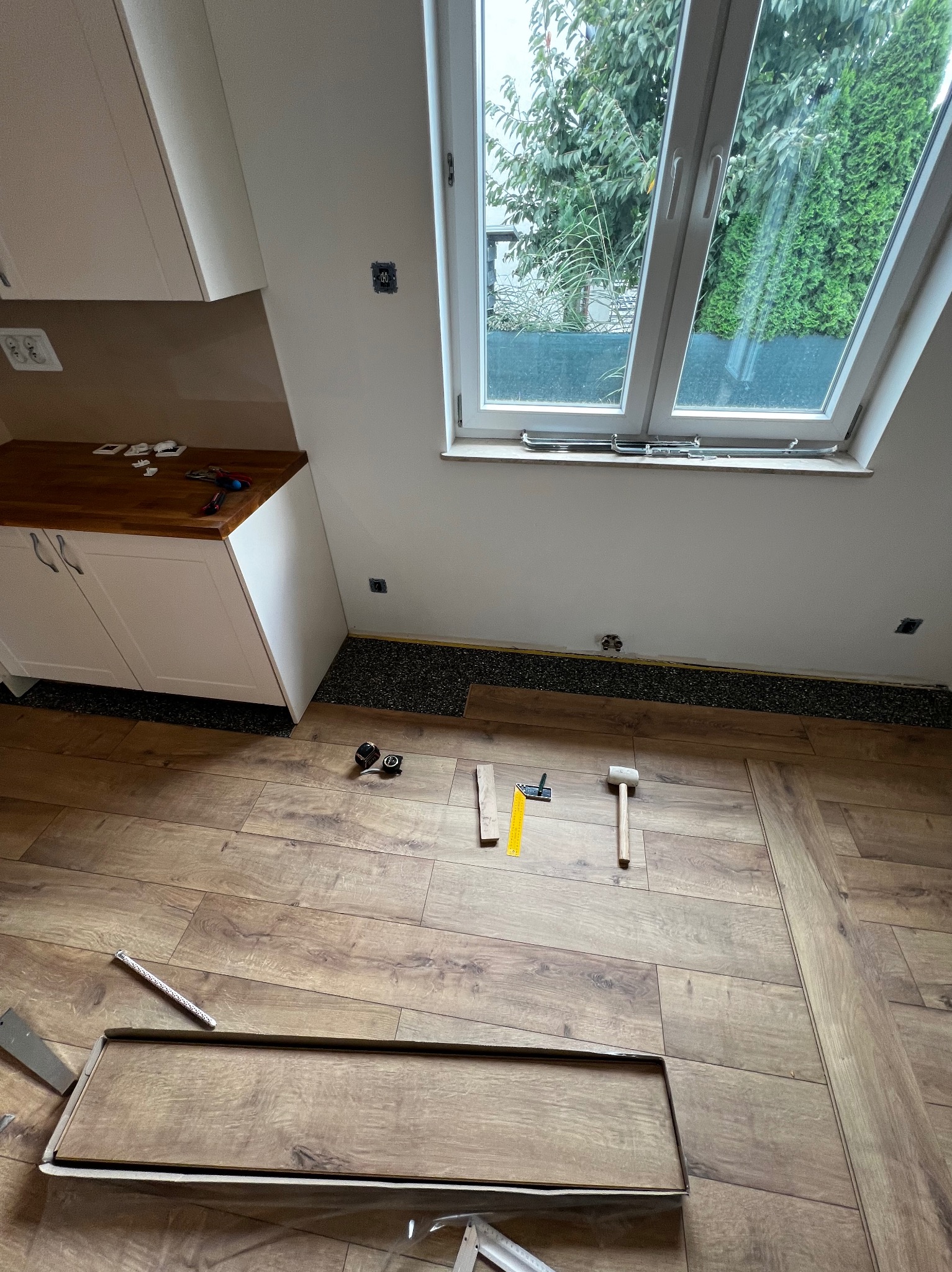 Układanie paneli podłogowych w pokoju z oknem dachowym. Widoczne narzędzia i fragmenty paneli, częściowo ułożona podłoga z brązowych paneli.