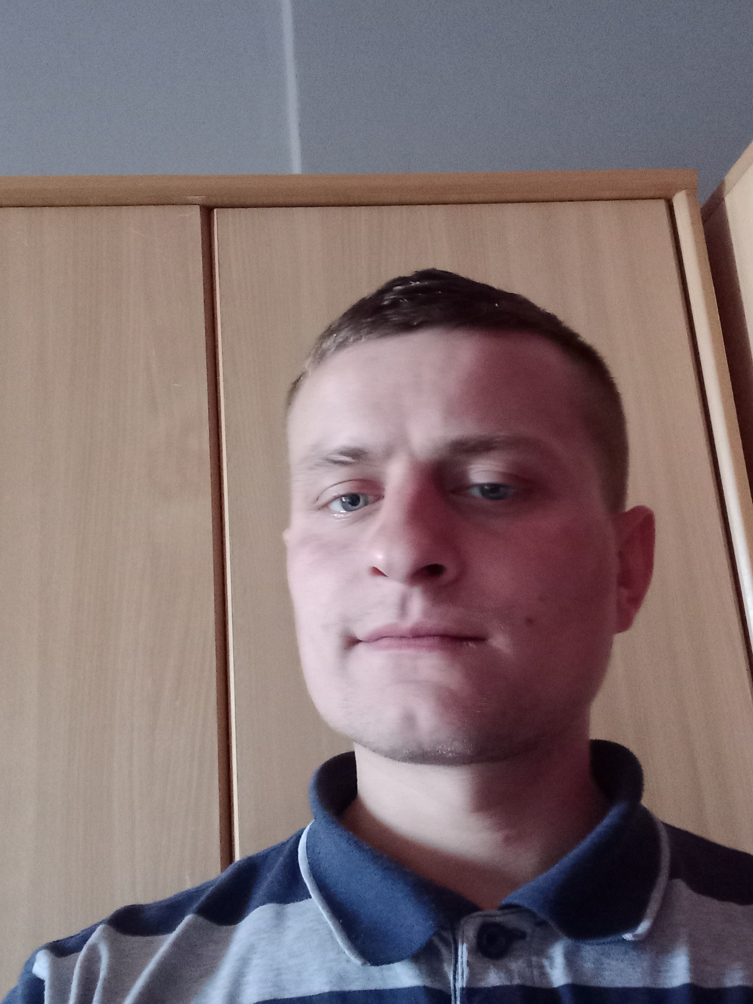 Portret mężczyzny w paski koszulce polo na tle jasnych drzwi szafy.