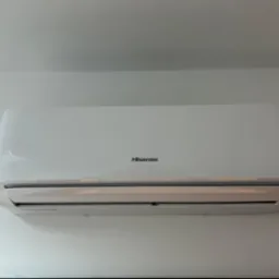 Biały klimatyzator Hisense zamontowany na białej ścianie, widoczny z dołu, z delikatnym światłem odbijającym się od obudowy.