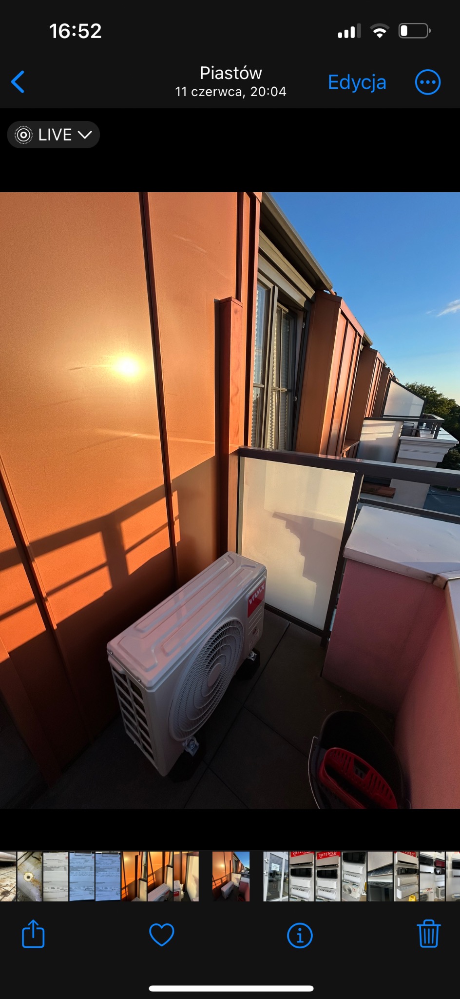 Biała jednostka zewnętrzna klimatyzatora Vivax na balkonie z pomarańczową ścianą w promieniach zachodzącego słońca, widok z góry.