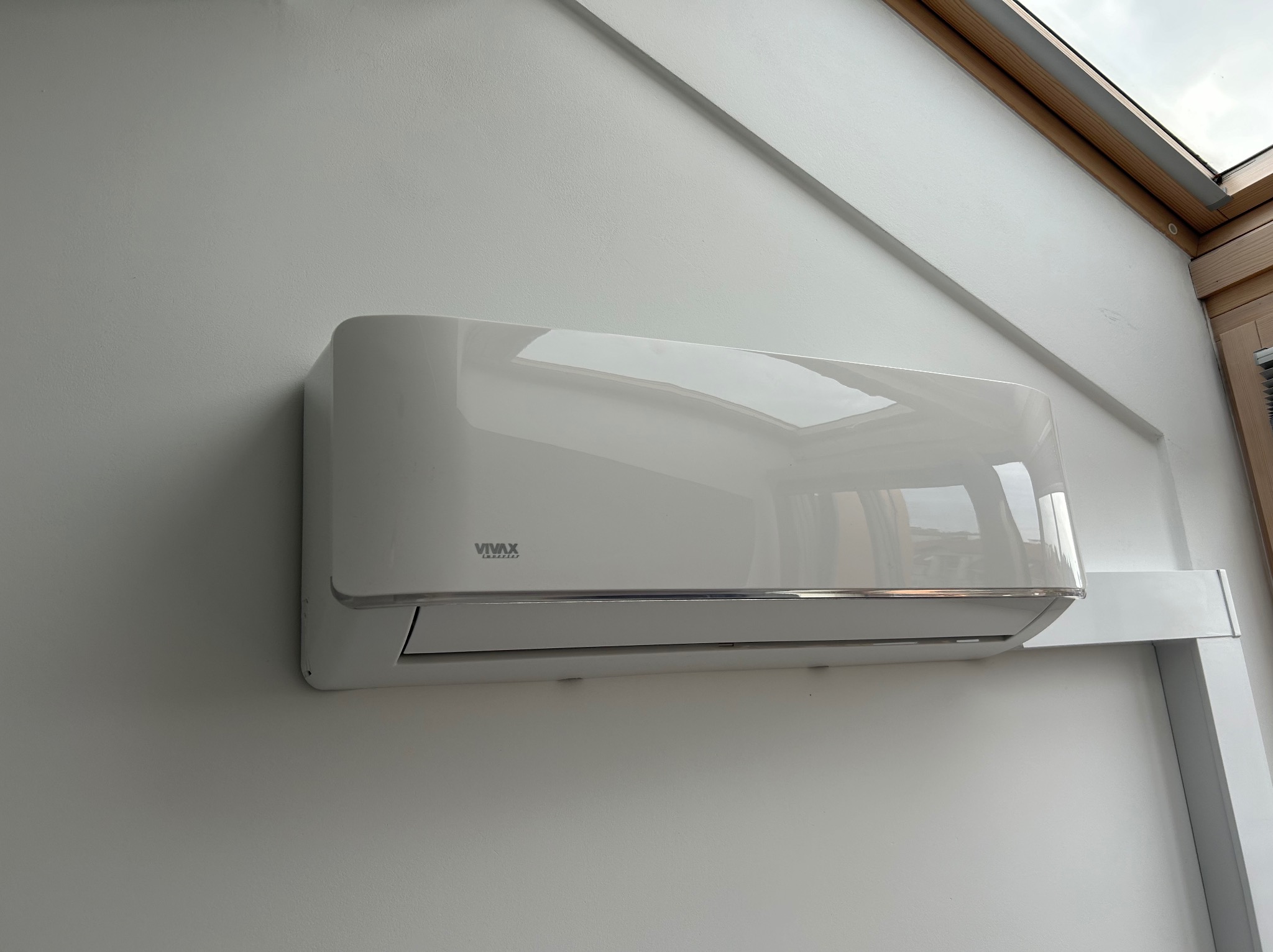 Biały klimatyzator VIVAX inverter zamontowany na białej ścianie w pomieszczeniu ze skośnym sufitem i oknem dachowym.