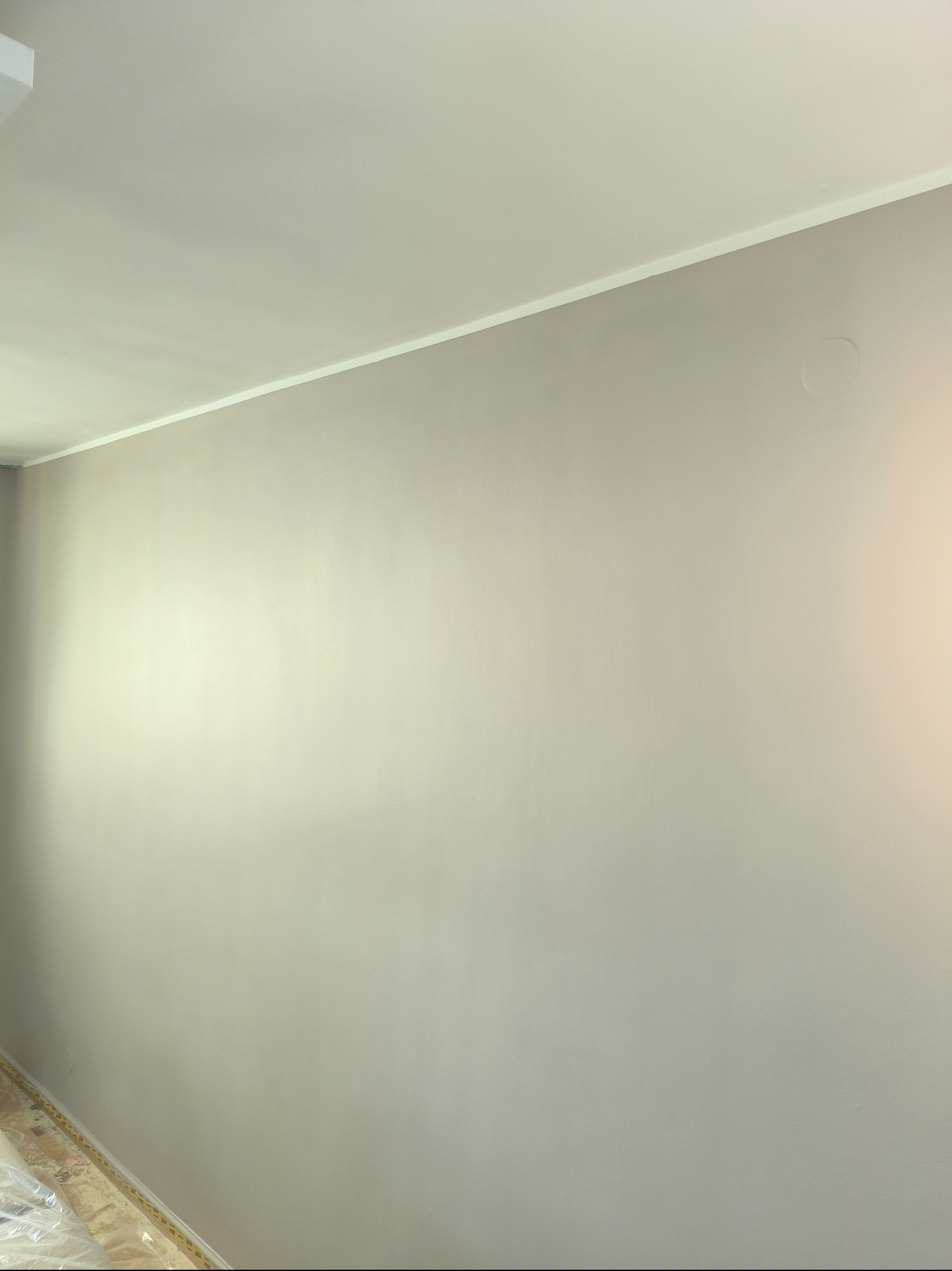 Świeżo pomalowana ściana w odcieniach szarości z widoczną listwą przypodłogową zabezpieczoną folią malarską.