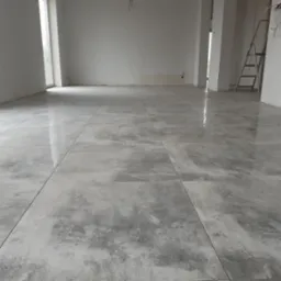 Nowa, duża podłoga wyłożona szarymi, matowymi płytkami w przestronnym, jasnym pokoju z drabiną w tle.