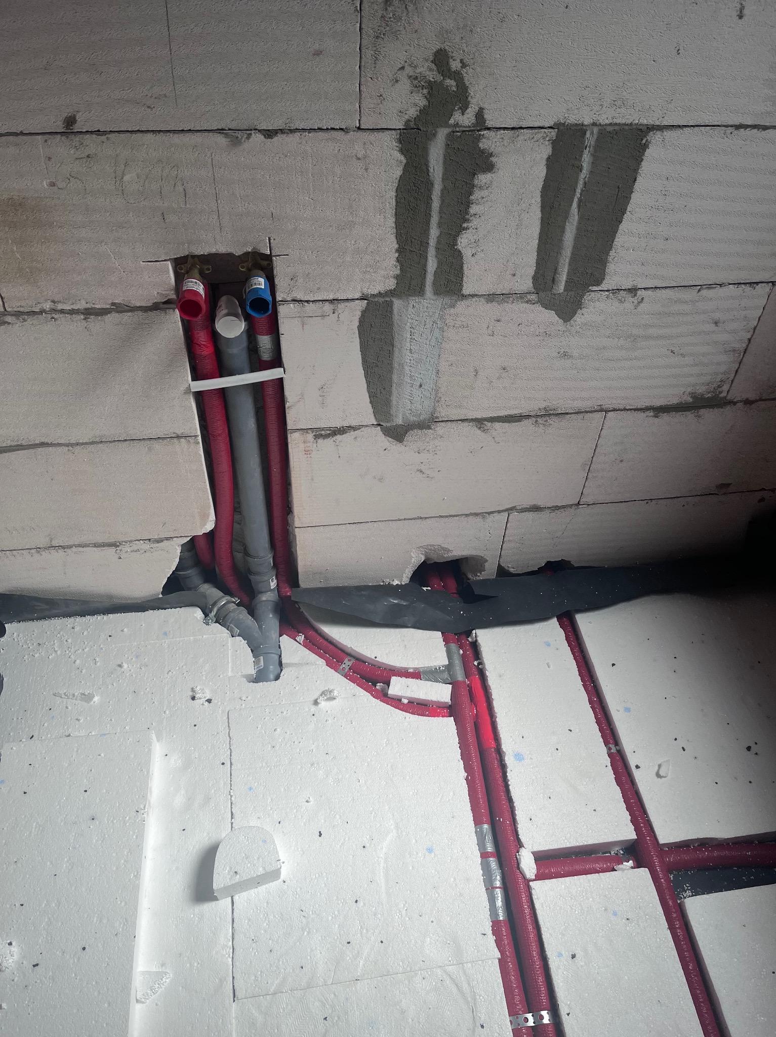 Instalacja wodna i kanalizacyjna w bruzdach ściennych i podłogowych przed wylewką, rury w izolacji, widoczne elementy mocujące.