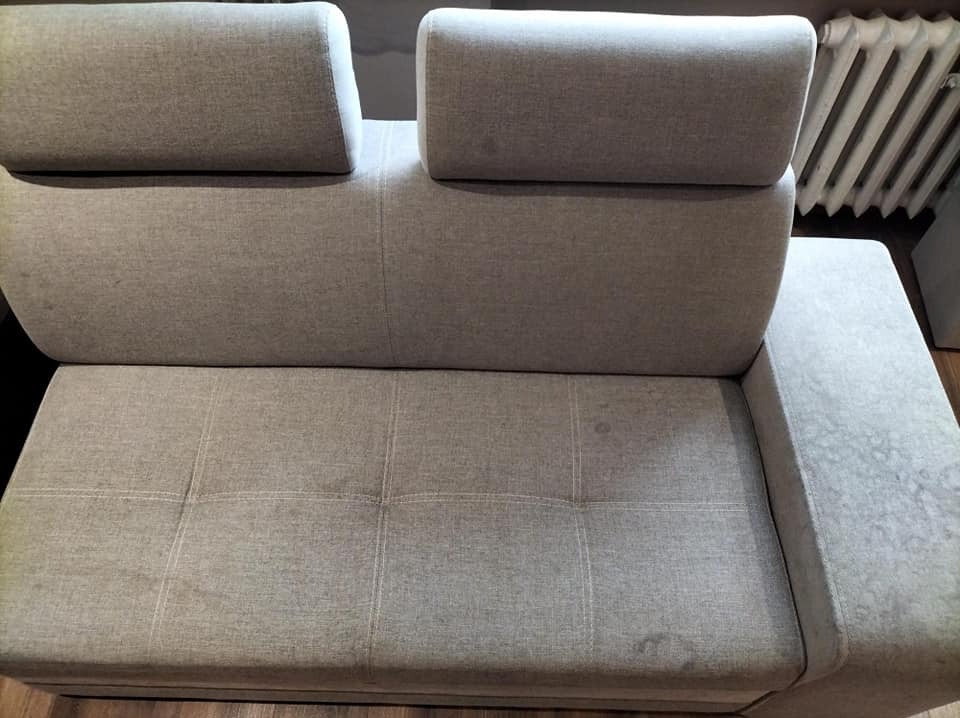 Szara, tapicerowana kanapa z widocznymi plamami na siedzisku i boku, sfotografowana z góry.