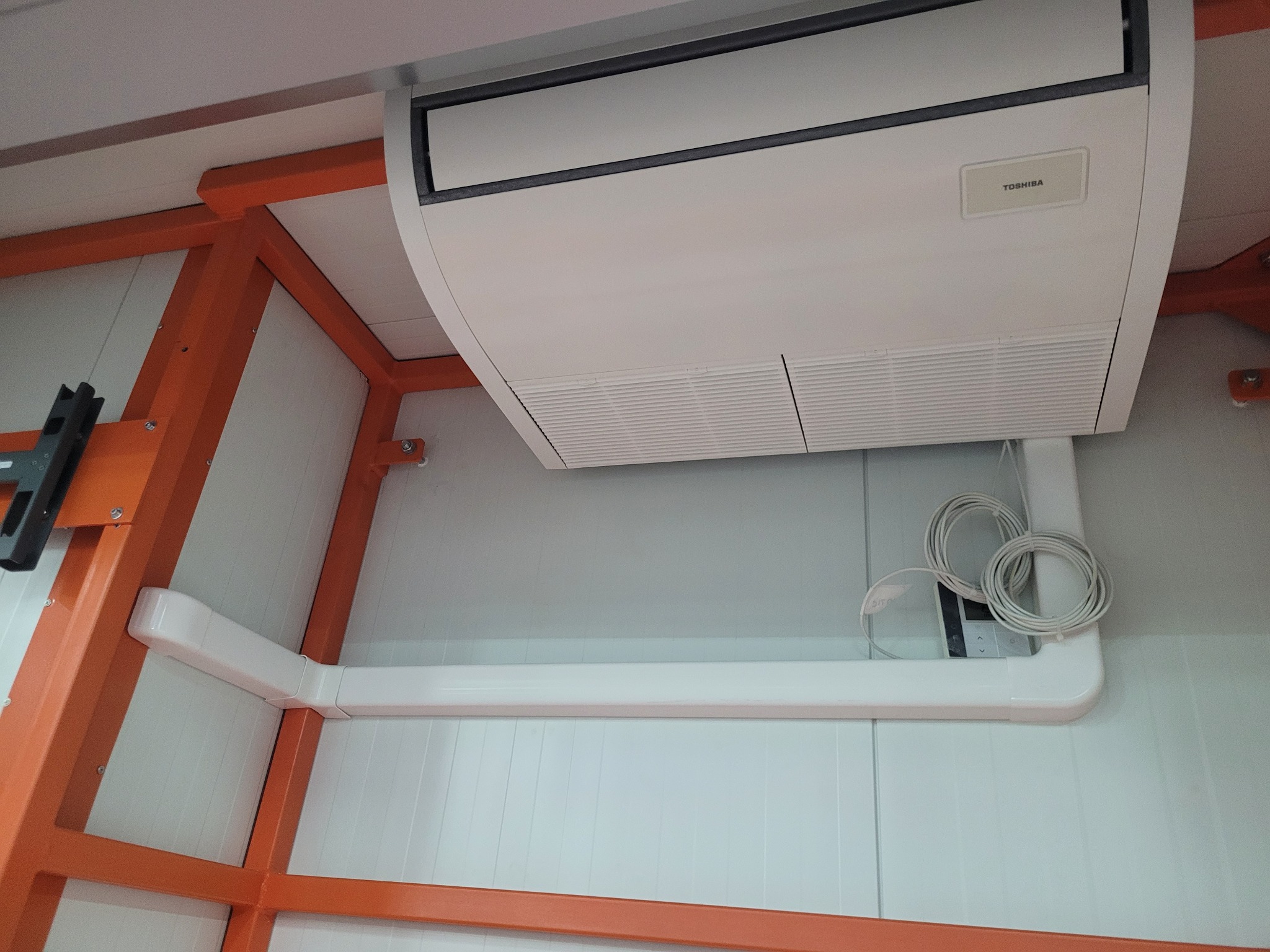Biała, sufitowa klimatyzacja Toshiba z widocznymi przewodami i elementami konstrukcyjnymi w pomieszczeniu. Widok z dołu.