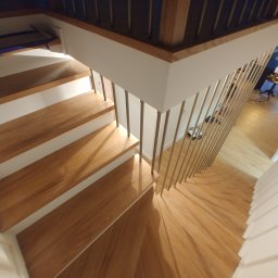 Bartłomiej Mucha - Nowoczesne schody z drewnianymi stopniami i metalową balustradą, widok z góry, jasne oświetlenie.