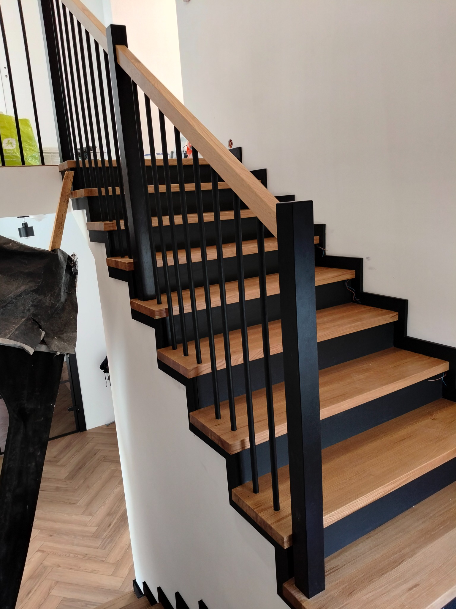 Nowoczesne schody z drewnianymi stopniami i czarnymi balustradami, widok z dołu, wykończenie w stylu minimalistycznym, podłoga w jodełkę.