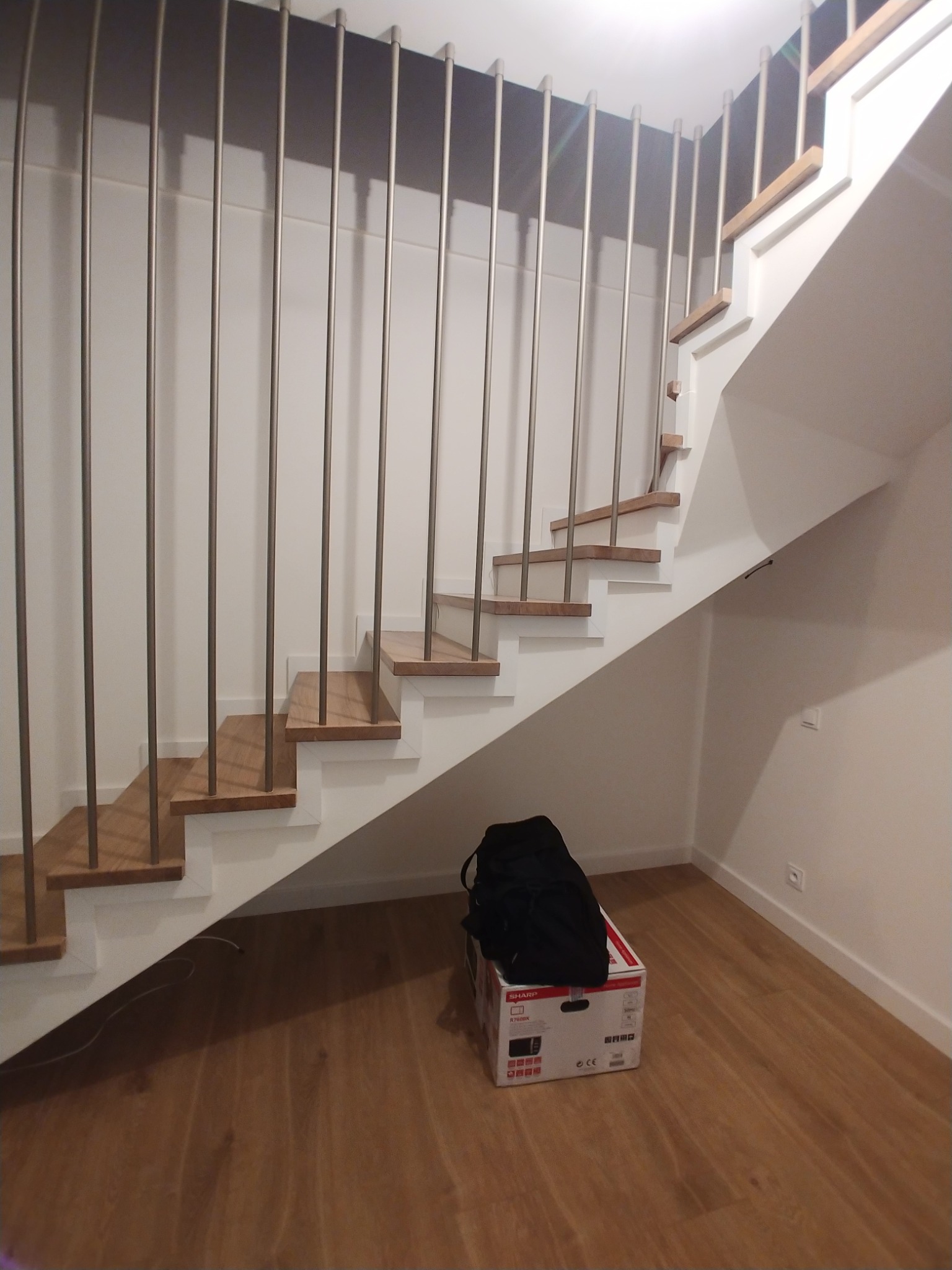 Białe schody z drewnianymi stopniami i metalowymi balustradami, widok z dołu, karton i czarna kurtka leżą pod schodami.