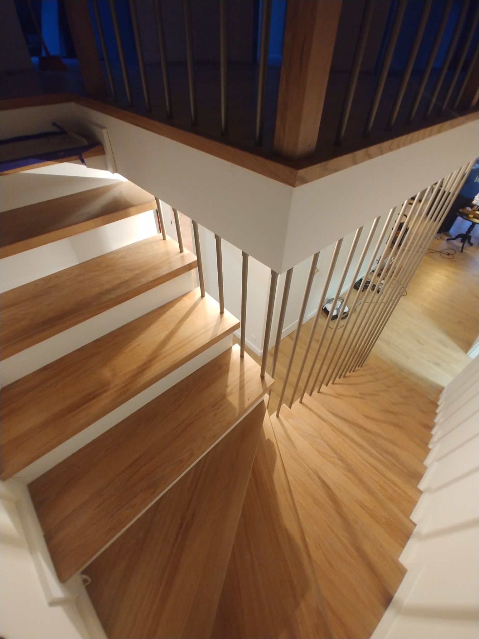 Nowoczesne schody z drewnianymi stopniami i metalową balustradą, widok z góry, jasne oświetlenie.