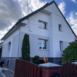 Dwukolorowa elewacja domu jednorodzinnego po dociepleniu, widoczne prace wykończeniowe przy cokole i pracownicy w trakcie malowania, Tomaszów Mazowiecki.