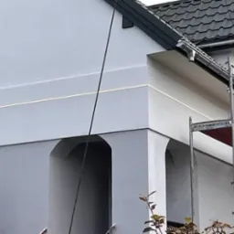 Jasnoszara elewacja domu po tynkowaniu w Tomaszowie Mazowieckim, widoczne rusztowanie i subtelne detale architektoniczne.