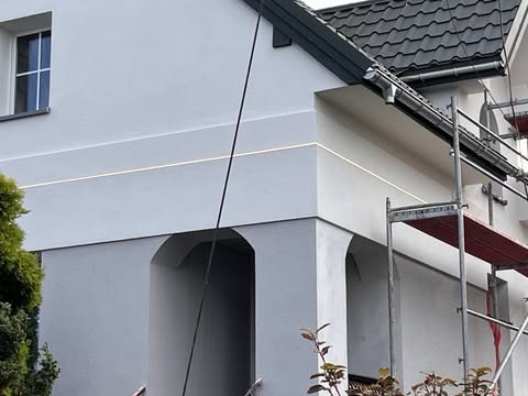 Jasnoszara elewacja domu po tynkowaniu w Tomaszowie Mazowieckim, widoczne rusztowanie i subtelne detale architektoniczne.
