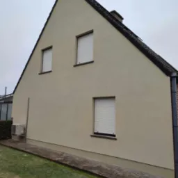 Świeżo wykończona elewacja domu jednorodzinnego z trzema oknami z roletami zewnętrznymi, widoczny fragment chodnika i trawnika oraz jednostka zewnętrzna klimatyzacji.