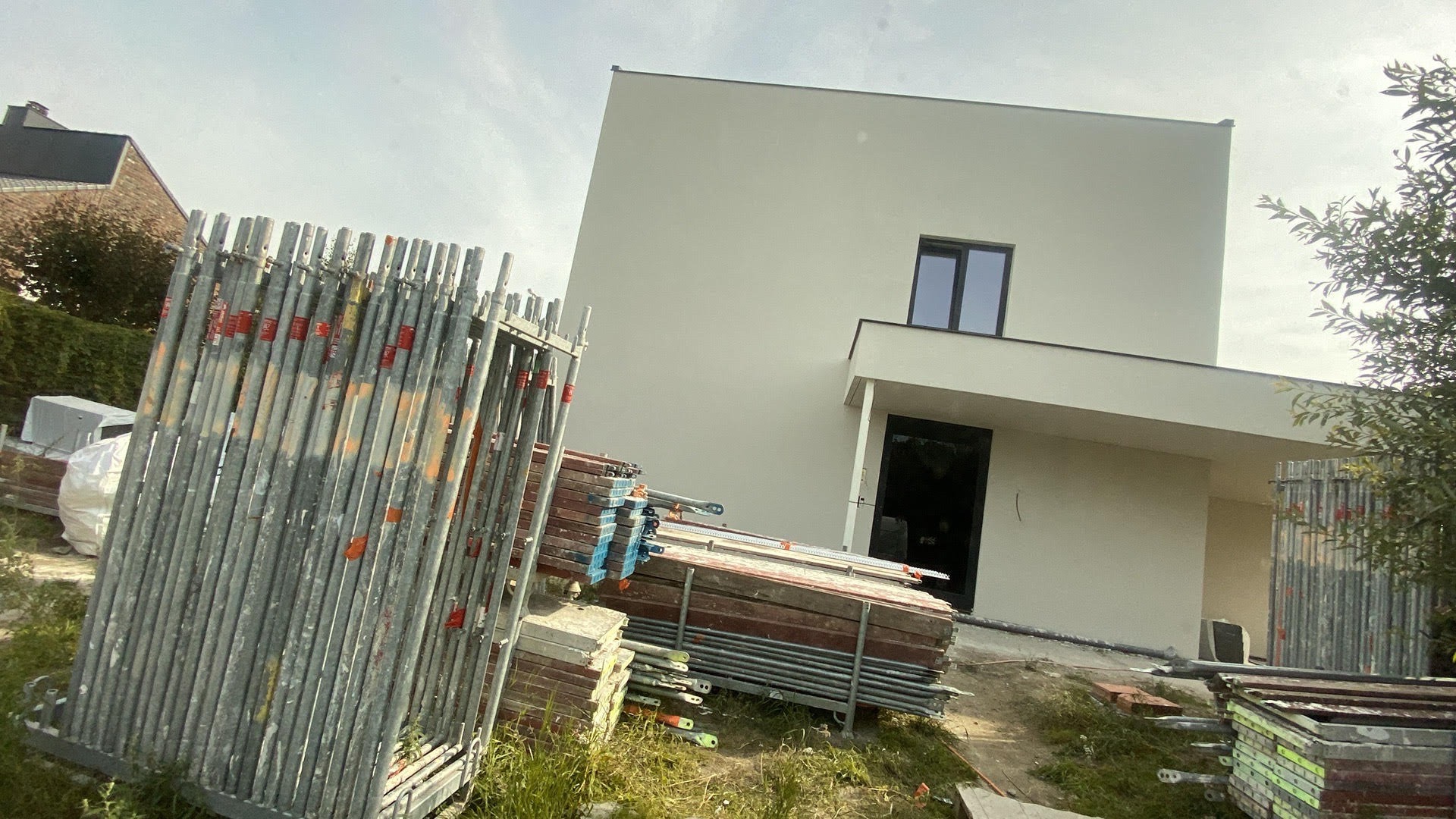 Nowoczesny dom jednorodzinny z jasną elewacją, widoczne rusztowania i materiały budowlane przygotowane do prac elewacyjnych.