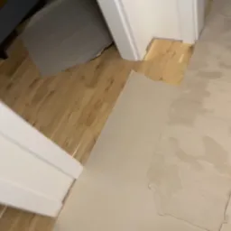 Przygotowanie podłoża pod panele: wyrównana podłoga z widocznymi śladami szpachlowania, fragment drewnianej podłogi i biała ościeżnica drzwiowa.