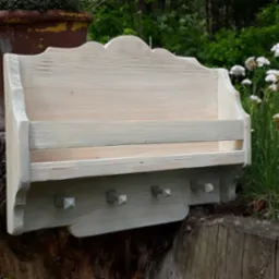 Drewniana półka w stylu rustykalnym, z haczykami i przegródkami, pomalowana na biało-szary kolor, ustawiona na pniu drzewa w ogrodzie.