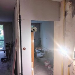 Remont marzeń - Wnętrze w trakcie montażu płyt gipsowo-kartonowych, widoczny profil pionowy, przewody elektryczne i prowizoryczne oświetlenie halogenowe.