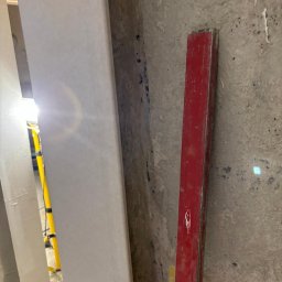 Remont marzeń - Ściana w trakcie remontu z widoczną łatą gipsową, starą czerwoną poziomicą i lampą budowlaną w tle.