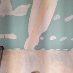 Remont marzeń - Niedokończona gładź na suficie z płyt gipsowo-kartonowych, widoczne łączenia płyt i plamy po szpachlowaniu, surowa ściana z widocznymi śladami farby i numerem '114,5'.